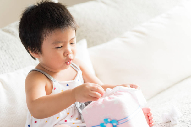 Chory mała dziewczynka azjatyckich wycierania lub czyszczenie nosa z tkanki siedzi na kanapie w domu. Koncepcja Medycyna i ochrona zdrowia. - Zdjęcie, obraz