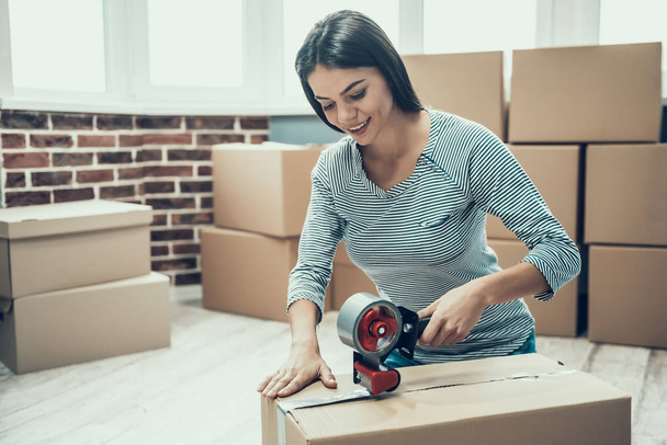 Young Smiling Woman Packing Cardboard Box at Home. Happy Beautiful Girl Preparing to Relocation by Packing Carton Boxes with Scotch Tape. Young Girl Moving to new Apartment - Φωτογραφία, εικόνα