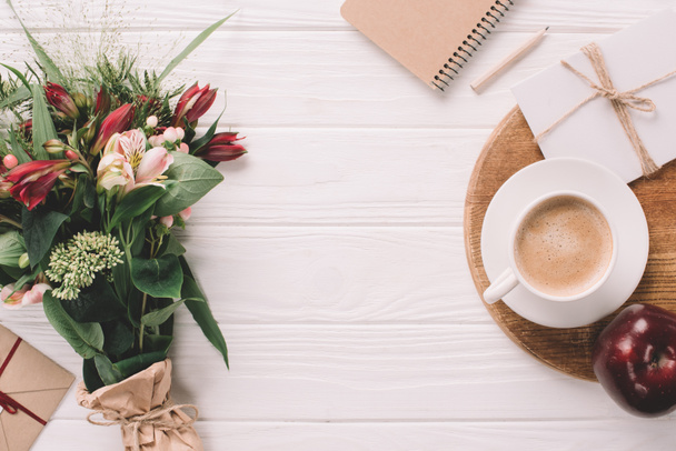 flat lay with wrapped bouquet of flowers, cup of coffee and notebook on white wooden tabletop - Photo, Image