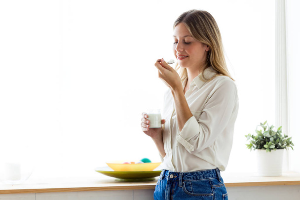 Shot of beautiful young woman eating yogurt at home - Foto, imagen
