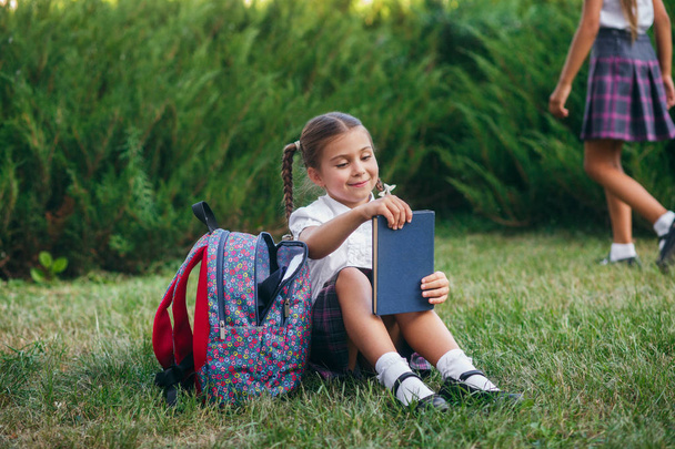 mała dziewczynka siedzi na trawie i czytanie książki. Uczniowie szkoły podstawowej. - Zdjęcie, obraz
