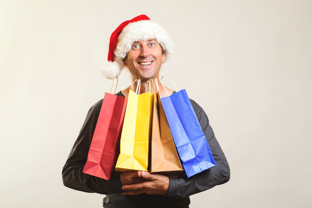 幸せサンタは、クリスマス プレゼントの買い物袋を保持しています。クリスマス ショッピング、販売と割引の概念。冬の休日。クリスマス帽子を楽しんでショッピング、分離された男。クリスマス ショッピング バッグ - 写真・画像