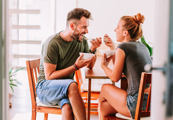 ダイニング ルームのテーブルで穀物の朝食を食べる若いカップル - 写真・画像