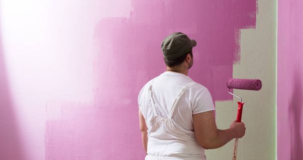 Young man is painting wall with painting roller - Foto, Imagem