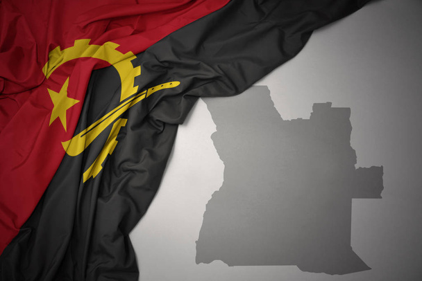 mává barevné státní vlajka Angoly na pozadí šedé mapy. 3D obrázek - Fotografie, Obrázek