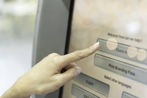 Zameldowanie przez siebie na maszynie kiosk. Zbliżenie: Kobieta palcem dotknąć ekranu kiosk maszyna do samoobsługowej odprawy w budynku lotniska. - Zdjęcie, obraz
