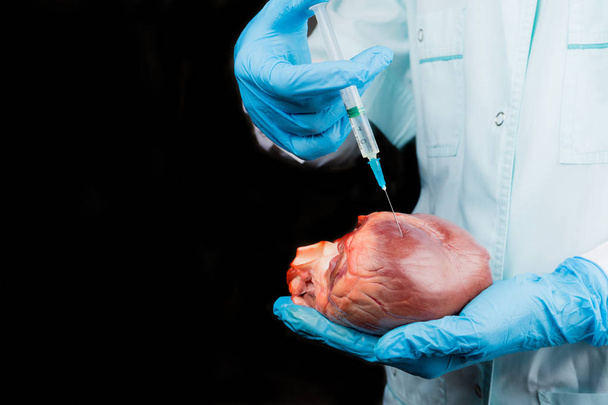 Το ιατρικό εργαζόμενο κάνει μια ένεση του φαρμάκου στην καρδιά. Σκούρο φόντο. Οριζόντια σύνθεση. - Φωτογραφία, εικόνα