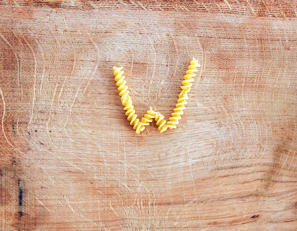 W letter done with pasta fusilli on a wooden chopping board - Photo, Image