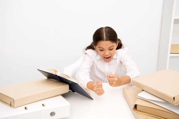 Studying hard. Girl child reads book while sit table white background. Schoolgirl studying and reading book. Kid school uniform angry irritated difficult task. Pupil emotional irritated expression - Foto, Imagem