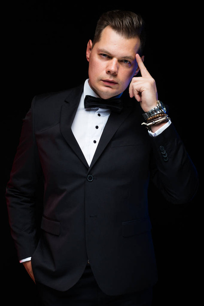 Portrait of confident handsome elegant stylish businessman with bow-tie showing on his brain on black background in studio - Photo, Image