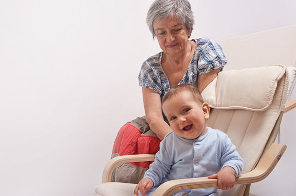 Vauva istuu tuolilla ja nauraa isoäidin kanssa
 - Valokuva, kuva