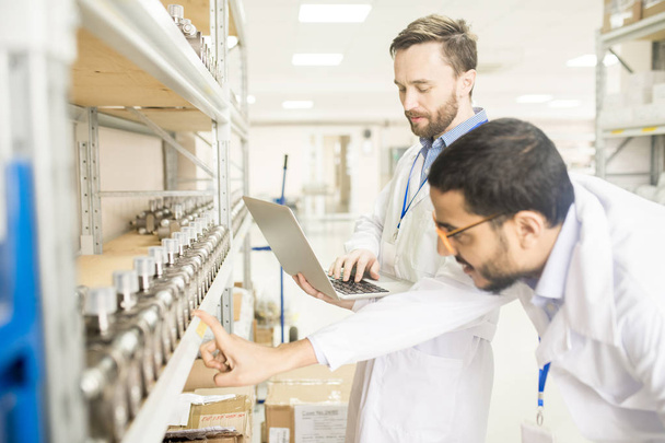 Multi-ethnic group of engineers wearing lab coats examining quality of measuring equipment while carrying out inspection at warehouse of modern factory - Photo, Image