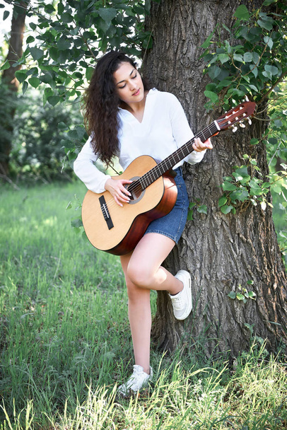 young woman walking in the forest and playing guitar, summer nature, bright sunlight, shadows and green leaves, romantic feelings - Foto, Imagen
