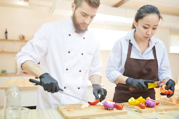 Portrait taille haute de deux cuisiniers professionnels travaillant dans la cuisine du restaurant coupant des légumes debout à la table en bois, espace de copie
 - Photo, image
