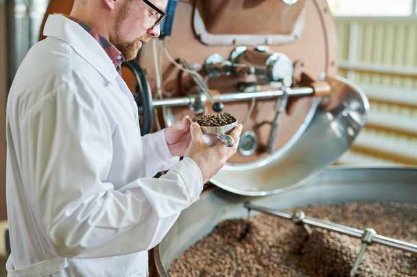 Портрет сучасного працівника, що носить лабораторне пальто, який тримає ложку бобів під час роботи у виробництві кави, копіювання простору
 - Фото, зображення