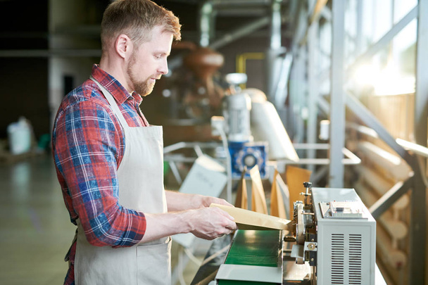 Side view portrait of modern bearded man wearing apron packing freshly roasted coffee beans in craft paper bags while working in artisan roastery house, copy space - Photo, Image