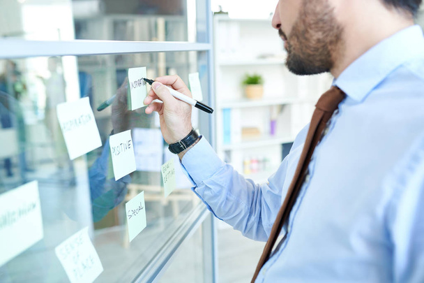 Crop homme d'affaires écrit sur des notes collantes composées de panneaux de verre travaillant dans un bureau moderne
.  - Photo, image