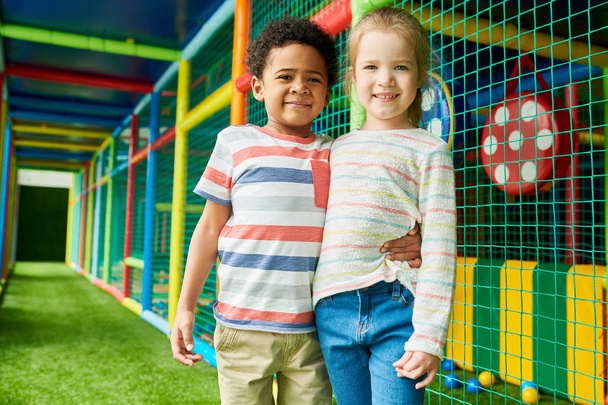 Colorato ritratto di ragazzo e ragazza felice posa abbracciandosi e guardando la fotocamera divertirsi nel centro giochi per bambini
 - Foto, immagini