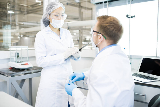 Retrato de dois jovens cientistas modernos vestindo jalecos discutindo o projeto enquanto trabalhavam em laboratório médico
 - Foto, Imagem