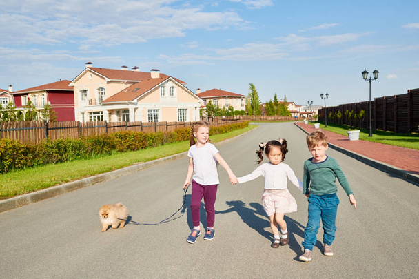 日光でカメラに向かって歩きながらペット犬の散歩 3 人の子供の完全な長さの肖像画 - 写真・画像