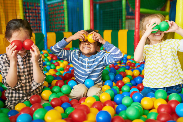 Retrato de tres niños pequeños y divertidos jugando en el hoyo de pelotas y disfrutando del tiempo en la zona de entretenimiento y juegos infantiles
 - Foto, imagen