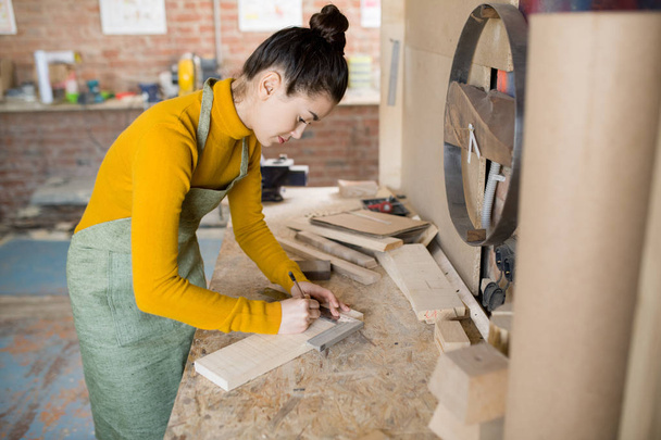 Porträt einer jungen Kunsthandwerkerin, die in einer modernen Tischlerei mit Holz arbeitet - Foto, Bild