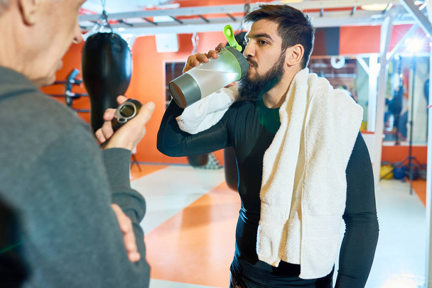 Ritratto in vita dell'uomo barbuto mediorientale che beve acqua dopo un duro allenamento nel club di arti marziali, copiare lo spazio
 - Foto, immagini