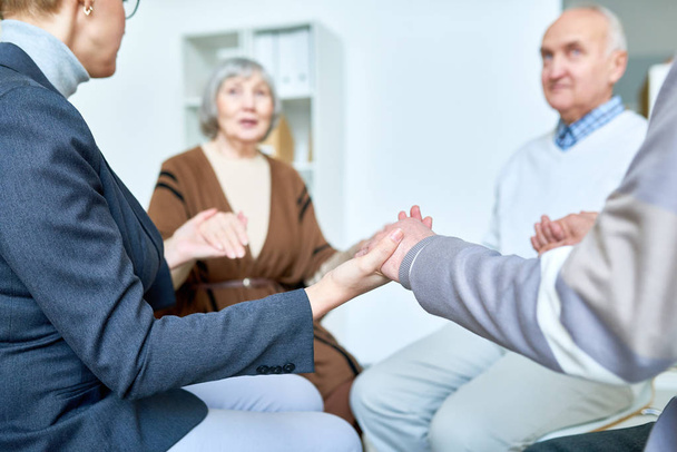 Gruppe von Senioren Händchen haltend in Gruppentherapie-Sitzung unter der Leitung einer Psychiaterin, Kopierraum - Foto, Bild
