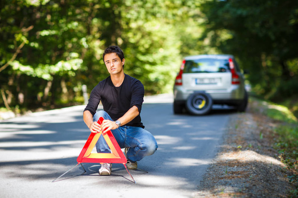 Handsome young man with his car broken down by the roadside, setting the safety triangle - Valokuva, kuva