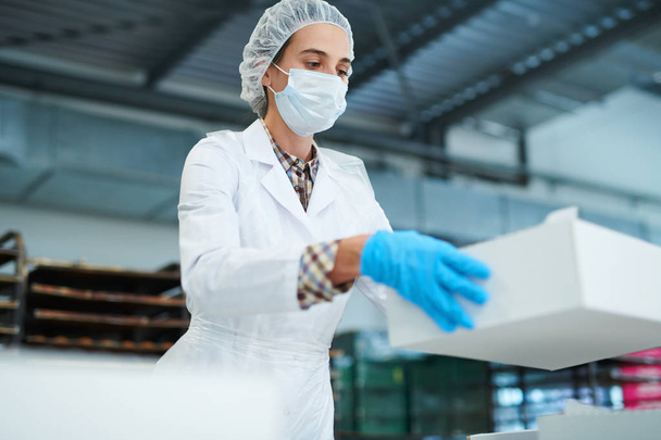 Employé de l'usine de confiserie debout dans un manteau blanc et tenant une boîte d'emballage en papier
. - Photo, image