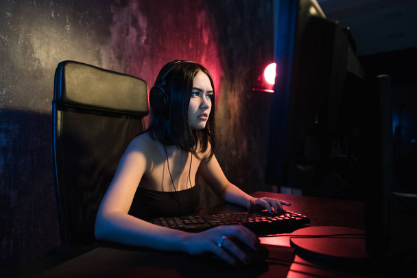 Concerned girl gamer in headphones playing network games preparing to participate in international competitions in e-sports. - Fotó, kép