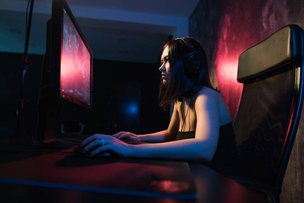 girl gamer in headphones and with a keyboard and mouse in her hands playing network games preparing to participate in international competitions in e-sports - Photo, Image