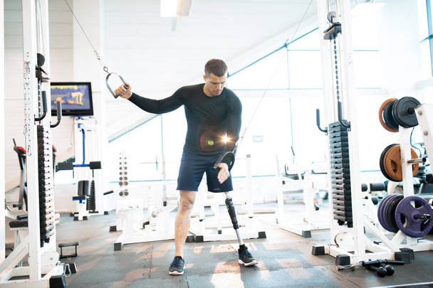 Retrato de comprimento total de homem musculoso bonito com perna protética trabalhando fora usando a máquina no ginásio moderno
 - Foto, Imagem