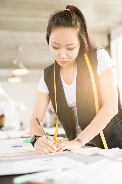 Pasu nahoru portrét cílené asijské ženy kreslení módní skicy stoje u krejčích stolu a pracovat v moderní design atelier prozářený sluncem - Fotografie, Obrázek