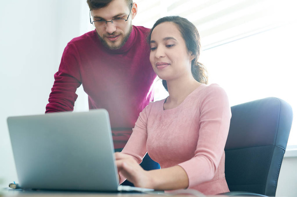 Positivo confiante empresária hispânica digitando texto no laptop, enquanto seu colega bonito examinar conter no escritório moderno
 - Foto, Imagem