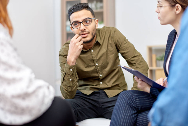 Portrait shot of handsome mixed-race man wearing eyeglasses participating in group therapy session at cozy office, friendly psychologist assisting her patients - Photo, Image