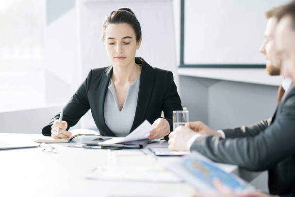 Portrait of confident young businesswoman listening to colleagues or partners sitting at meeting table in conference room - Photo, Image