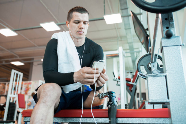 Young disabled man listening to music on his phone after training - Photo, Image