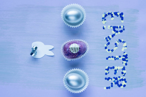 Immagine di sfondo di tre uova di cioccolato dipinte di perla che giacciono in fila con la parola PASQUA disposti in paillettes scintillanti, primo piano
 - Foto, immagini
