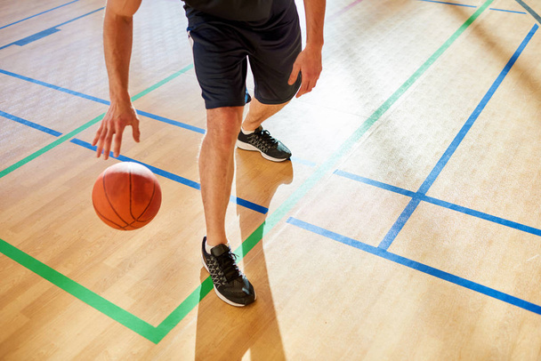 Баскетболист капает мяч на полу корта во время матча
.  - Фото, изображение