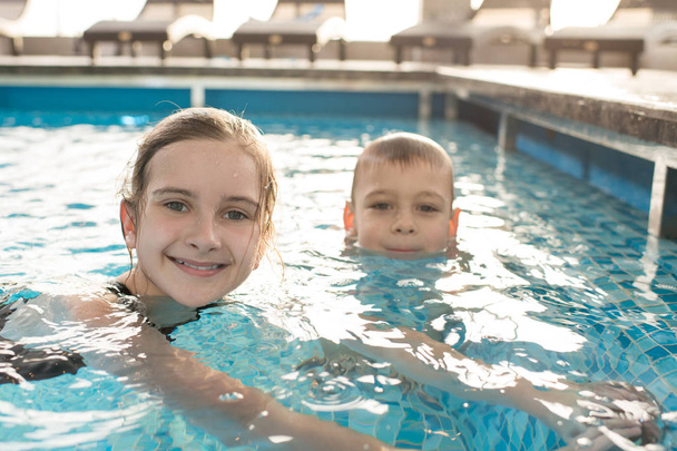 Retrato de niños lindos positivos con el pelo mojado sentado en el agua caliente de la piscina y relajarse juntos
 - Foto, imagen