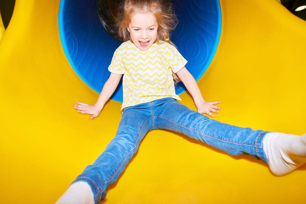 黄色のプラスチック製のスライドを下って行くと、遊び場で楽しんで、フラッシュで撮影しながら興奮して叫んで幸せな少女の肖像画 - 写真・画像
