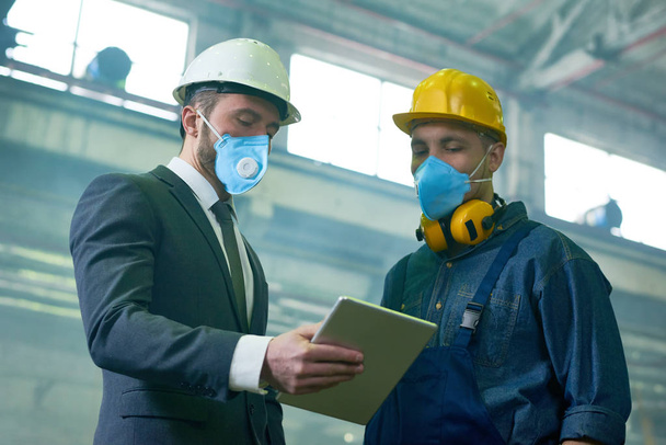 Portrait of two engineers wearing protective masks and hardhats working  at hazardous industrial plant, copy space - Photo, Image