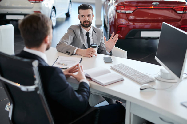 Muotokuva kypsä parrakas liikemies puhuu myyntipäällikkö istuu pöydän toisella puolella auton jälleenmyyntisopimuksen näyttelytila
 - Valokuva, kuva