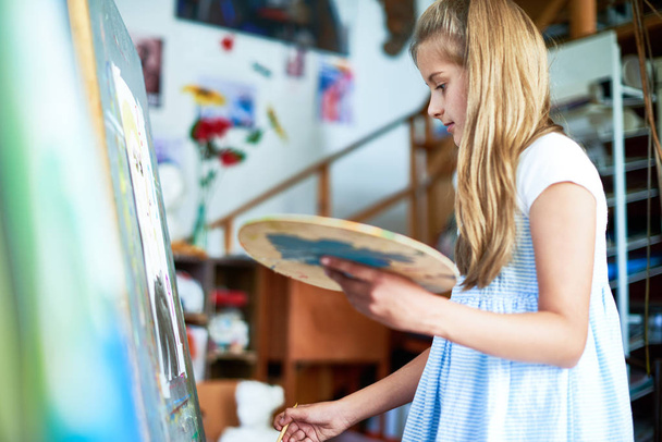 サイド ビュー イーゼル色パレットを保持している、美術の授業で絵を描いているかなり 10 代の少女像 - 写真・画像