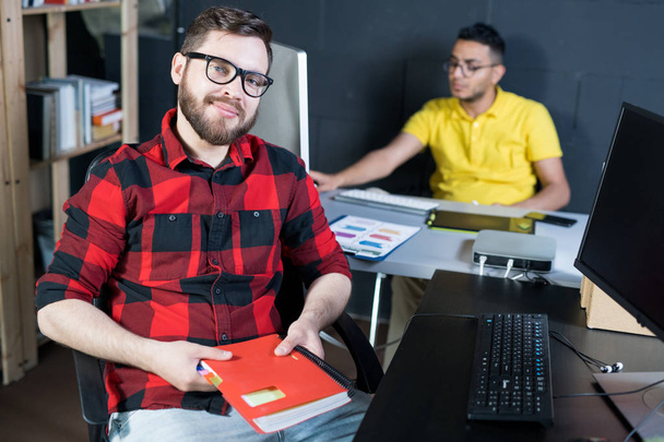 メガネとそれで机に座って赤いシャツを身に着けている現代の若い男の肖像コピー スペース創造的な開発者チームの事務所 - 写真・画像