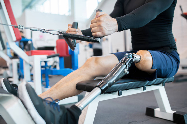 Низкий разрез крупным планом неузнаваемого мускулистого человека с протезной ногой с помощью весовой машины во время тренировки в тренажерном зале
 - Фото, изображение