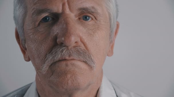 Gesicht eines älteren Mannes mit Schnurrbart blickt vor weißem Hintergrund in die Kamera - Filmmaterial, Video