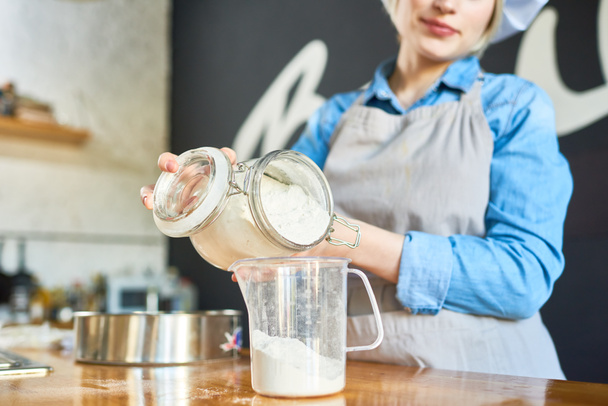 Female cook pouring flour into a measuring cup - Photo, Image