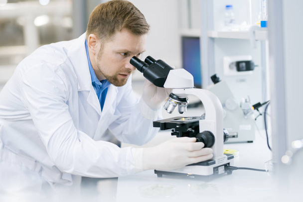 Portret młodego naukowca patrząc w mikroskopu podczas pracy na badania w laboratorium medyczne - Zdjęcie, obraz